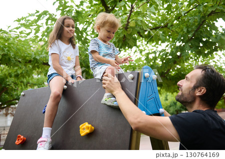 Father Helping Kids Play on Outdoor Climbing Structure in Playground 130764169