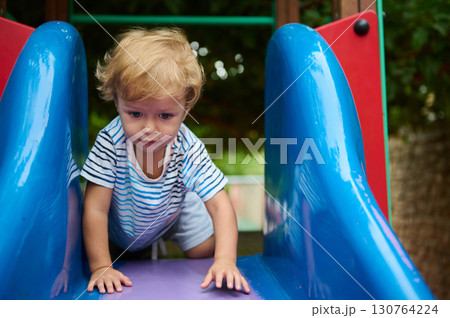 Young Child Crawling on a Colorful Playground Slide Outdoors Young Child Crawling on a Colorful Playground Slide Outdoors 130764224