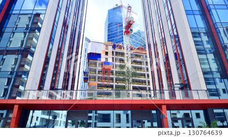 Crane on the construction site in a site surrounded by the high buildings. Office building under construction in the vicinity of high apartment buildings and office building. 130764639