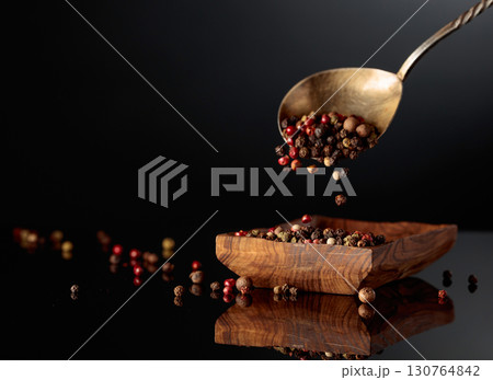 Black, red, white, and allspice peppercorns is poured in wooden dish. 130764842
