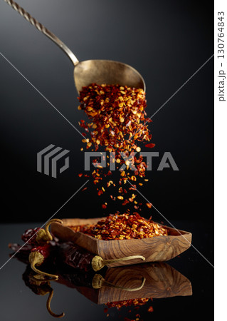 Dry red chili peppers and crushed chili flakes on a black reflective background. 130764843
