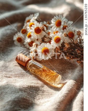 Essential oil bottle lying near bouquet of chamomile flowers on linen fabric 130765289