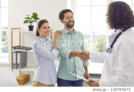 Male family therapist shaking hands with a young happy married couple standing in office. 130765673