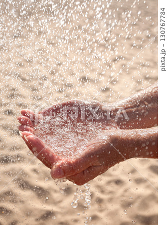 Hands catching sparkling water droplets over sandy beach 130767784