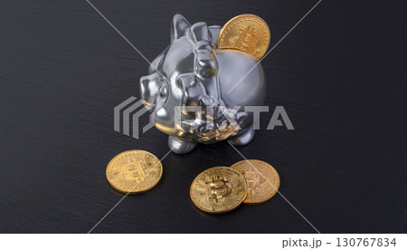 Silver piggy bank receiving golden bitcoin on black background 130767834