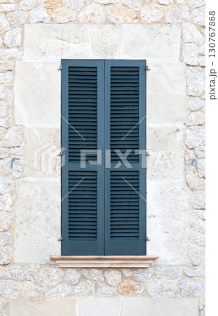 Closed blue wooden shutters on a traditional stone wall facade Closed blue wooden shutters on a traditional stone wall facade 130767868