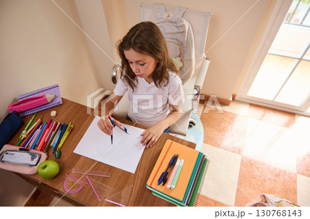 Young Girl Drawing with Compass at Desk in Brightly Lit Room 130768143
