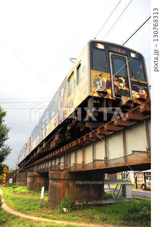 石見神楽のラッピンング列車（キハ126系ディーゼル気動車）が市街地の背の低い橋桁の鉄橋を通過する光景 130768313
