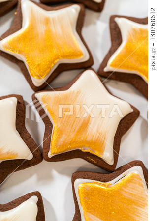 Close-up of a gingerbread star cookie painted with shimmering gold luster dust over smooth royal icing, highlighting the fine details. Close-up of a gingerbread star cookie painted with shimmering gold luster dust over smooth royal icing, highlighting the fine details. 130768612