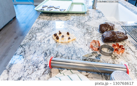 In a contemporary white kitchen, gingerbread cookie dough is skillfully rolled out, setting the stage for a delightful holiday treat. In a contemporary white kitchen, gingerbread cookie dough is skillfully rolled out, setting the stage for a delightful holiday treat. 130768617