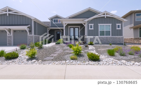 A modern gray house with symmetrical architecture and clean lines is landscaped with small decorative plants and stones. The large concrete driveway adds to the clean visual appeal. A modern gray house with symmetrical architecture and clean lines is landscaped with small decorative plants and stones. The large concrete driveway adds to the clean visual appeal. 130768685