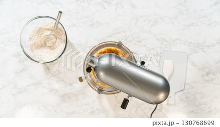 Overhead view of a stand mixer and prepared ingredients for Amber Gingerbread Cookie Dough, ready for mixing. Dry and wet ingredients are arranged around the mixer on a marble surface. Overhead view of a stand mixer and prepared ingredients for Amber Gingerbread Cookie Dough, ready for mixing. Dry and wet ingredients are arranged around the mixer on a marble surface. 130768699