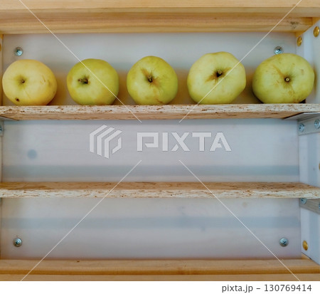 Five green apples arranged in a minimalist style on a wooden shelf representing order and simplicity with copy space 130769414