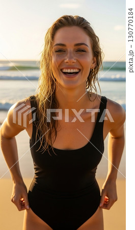 Happy beautiful woman in a black swimsuit laughing on the beach during a golden sunset 130770184