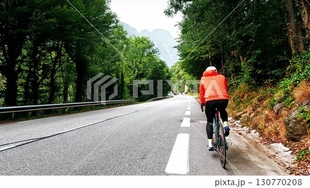 Cyclist riding on a mountain road in forest with following camera view, French Alps 130770208