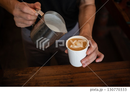 Barista holding a paper cup of latte coffee after pouring steamed milk to making latte art. Barista holding a paper cup of latte coffee after pouring steamed milk to making latte art. 130770333