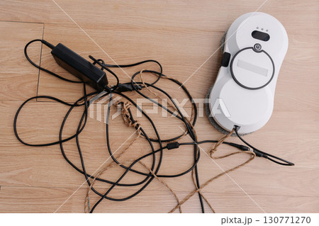Top view of modern white window cleaning robot lying on floor, resting beside charger and safety rope, preparing for efficient window cleaning tasks with advanced technology and automation at home. 130771270