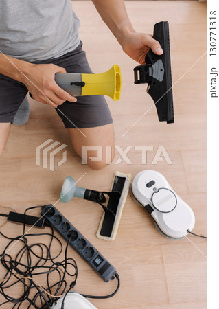 Janitor male preparing cordless window cleaning appliances and robot vacuum cleaner for cleaning large window in office building, focus on window cleaning tools. Concept of household cleanliness. Janitor male preparing cordless window cleaning appliances and robot vacuum cleaner for cleaning large window in office building, focus on window cleaning tools. Concept of household cleanliness. 130771318