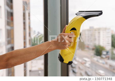 Close-up cropped shot of unrecognizable cleaning service worker using modern cordless vacuum cleaner for washing windows in high-rise building, ensuring streak-free cleanliness and hygiene. 130771348