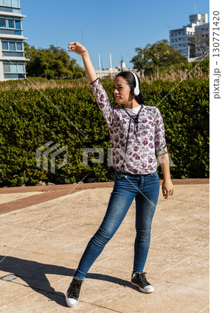 Young latin woman dancing with headphones in urban park 130771420