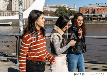 Three young women talking and smiling by the river in puerto madero, buenos aires Three young women talking and smiling by the river in puerto madero, buenos aires 130771444