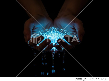 Cupped hands holding magical glowing blue water with dripping light particles on a dark background 130771634