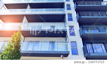 Modern apartment building with balconies and greenery. Beautiful view of real estate buildings in summer. Walking area with trees and grass. Modern residential buildings in the public green area.  130771723