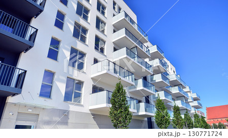 Modern apartment building with balconies and greenery. Beautiful view of real estate buildings in summer. Walking area with trees and grass. Modern residential buildings in the public green area.  130771724