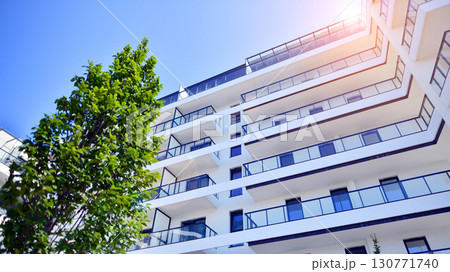 Modern apartment building with balconies and greenery. Beautiful view of real estate buildings in summer. Walking area with trees and grass. Modern residential buildings in the public green area. Modern apartment building with balconies and greenery. Beautiful view of real estate buildings in summer. Walking area with trees and grass. Modern residential buildings in the public green area. 130771740