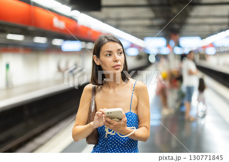Young girl standing on subway platform with phone in hand Young girl standing on subway platform with phone in hand 130771845