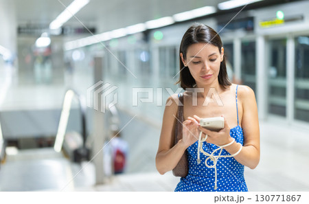 Young girl standing at train station with phone in hand 130771867