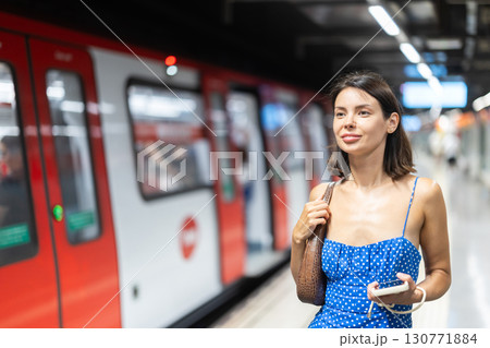 Happy young girl standing on subway platform with phone in hand 130771884
