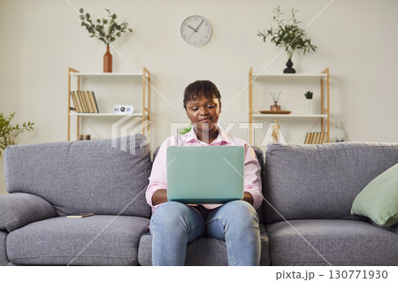 Young African American woman sits on couch with laptop, considering work project or financial issues 130771930