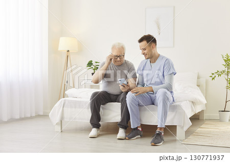 Doctor Or Caregiver With Elderly Man Using Smartphone For Online Entertainment Doctor Or Caregiver With Elderly Man Using Smartphone For Online Entertainment 130771937