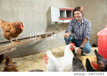Middle aged european male farm worker hand-feeding hens 130772503