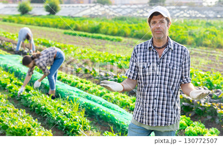 Positive man owner of plantation garden is resting standing after work and tasks. Positive man owner of plantation garden is resting standing after work and tasks. 130772507