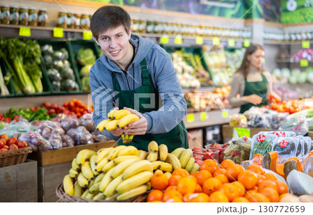Young salesman lays out bananas on counter 130772659