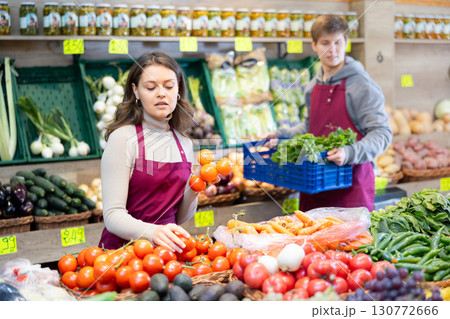 Saleswoman in an apron puts ripe tomatoes on supermarket window Saleswoman in an apron puts ripe tomatoes on supermarket window 130772666
