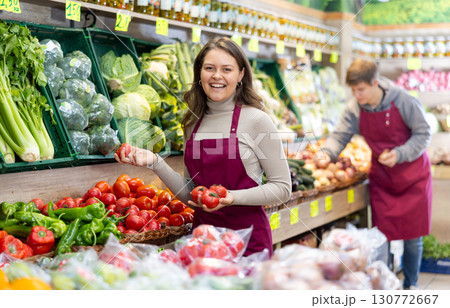 Young female seller holding tomatoes standing by counter in grocery market Young female seller holding tomatoes standing by counter in grocery market 130772667