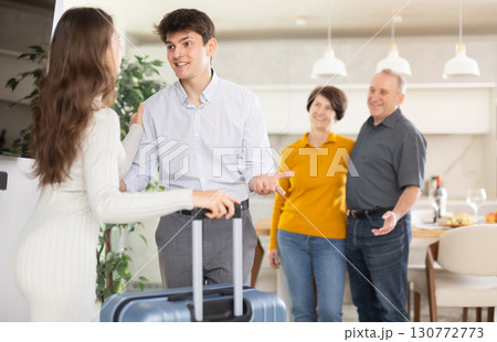 Happy young girl coming to meet boyfriend's family. Elderly mother, father and young guy joyfully greeting at door Happy young girl coming to meet boyfriend's family. Elderly mother, father and young guy joyfully greeting at door 130772773