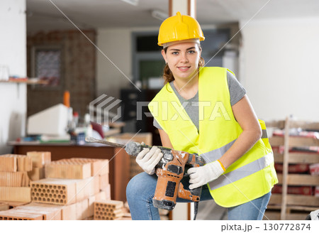 Portrait of positive woman builder standing in construction site 130772874