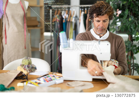 Man tailor sews on sewing machine in workshop Man tailor sews on sewing machine in workshop 130772875