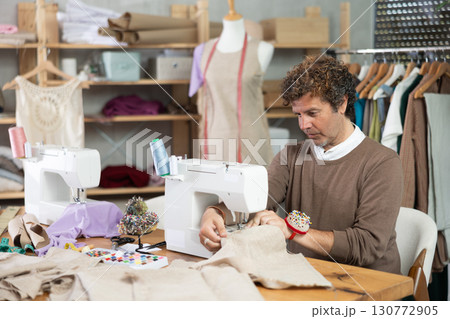 Man tailor sews on sewing machine in workshop 130772905