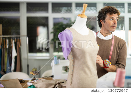 Man tailor connects parts of dress on mannequin Man tailor connects parts of dress on mannequin 130772947