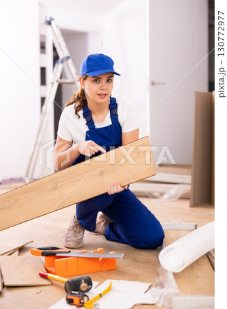 Repair in the room - woman puts laminate on the floor and checks horizontal level 130772977