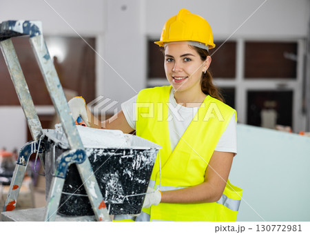 Portrait of woman painter in a protective helmet and vest with paint roller Portrait of woman painter in a protective helmet and vest with paint roller 130772981