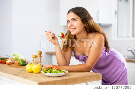 Smiling young woman eating salad at home Smiling young woman eating salad at home 130773096