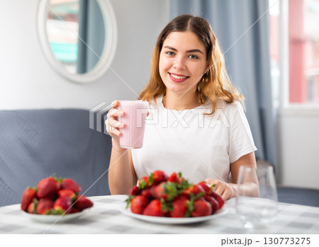 Young woman eating strawberry at home 130773275