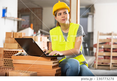 Female contractor using laptop to check plan of building under construction 130773278
