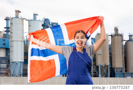 Positive young woman in workwear holds the national flag of Norway Positive young woman in workwear holds the national flag of Norway 130773287